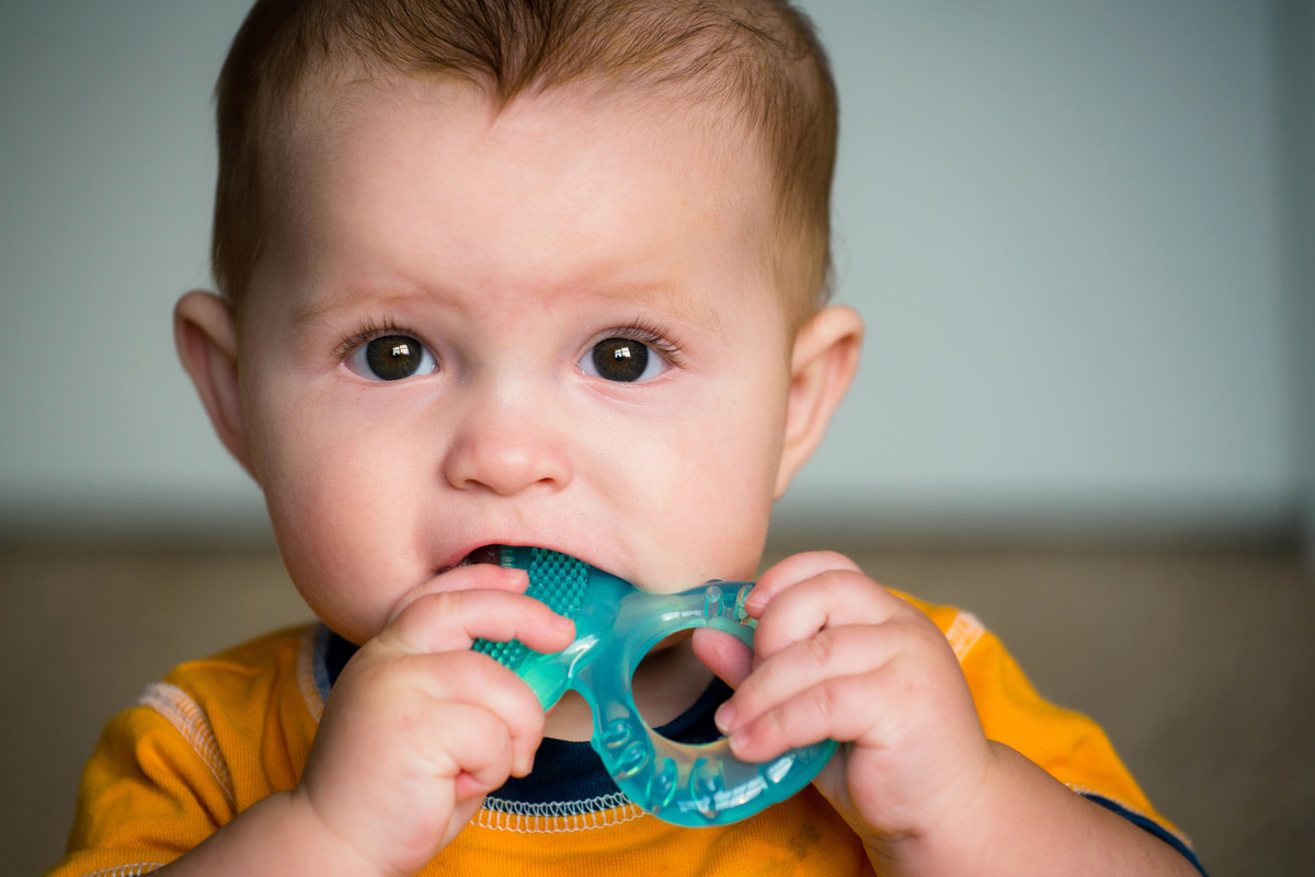 A baby chews a teething toy, a generally safe way to alleviate teething pain.